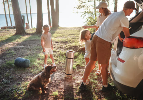 família a descarregar a mala do carro na natureza.