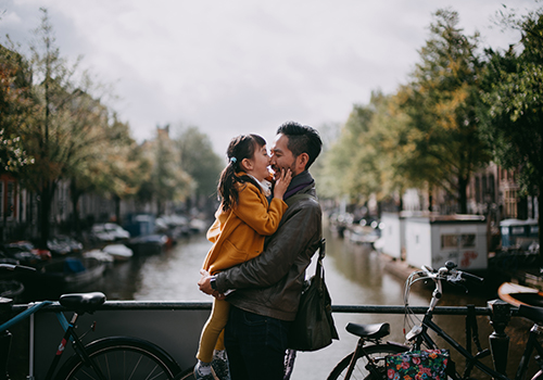 pai com a filha ao colo enquanto passeiam numa ponte de um canal em Amesterdão.